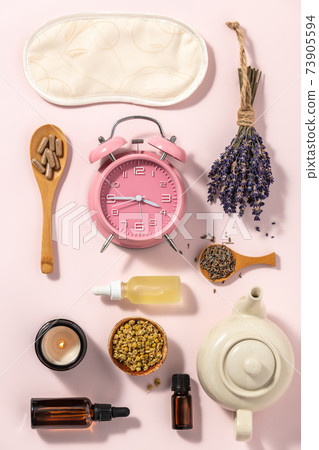 Herbal medicine for treat depression and insomnia concept. Alarm clock, medicine herbs, capsules, camomile tea and aromatherapy oil on pink background, flat lay 73905594