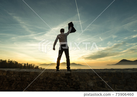 Businessman holding aloft his jacket at sunset 73906460