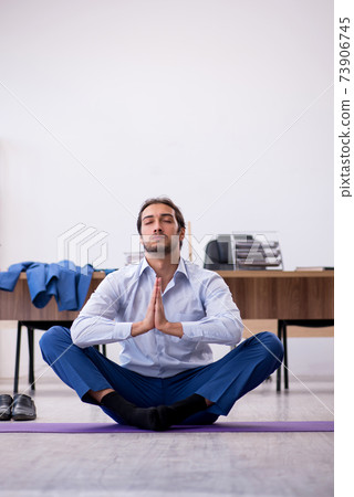 Young male employee doing sport exercises during break 73906745