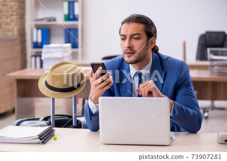 Young male employee preparing for trip in the office 73907281