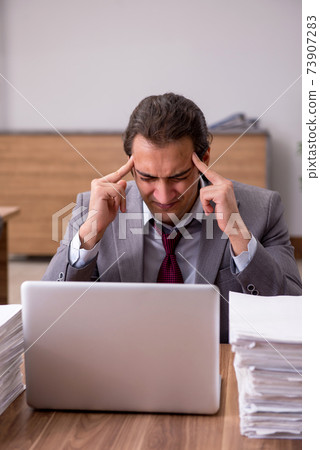 Young male employee unhappy with excessive work in the office 73907283