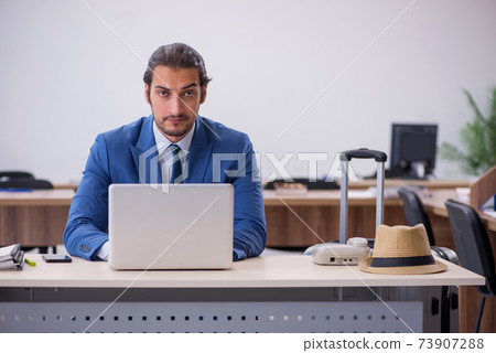 Young male employee preparing for trip in the office 73907288