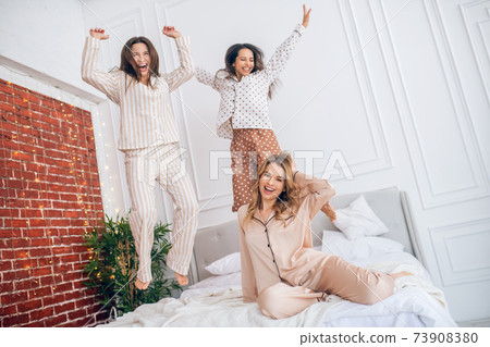 Three young girls jumping on bed and feeling amazing 73908380