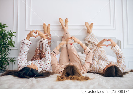 Three girls lying in bed with their legs up 73908385