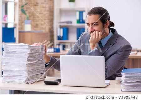 Young male employee unhappy with excessive work in the office Young male employee unhappy with excessive work in the office 73908448