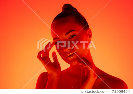 Handsome woman's portrait isolated on orange gradient studio background in neon light, monochrome 73909404