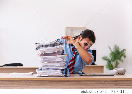 Young male employee unhappy with excessive work in the office Young male employee unhappy with excessive work in the office 73913323