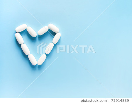White pills in the shape of heart on soft blue background. 73914889