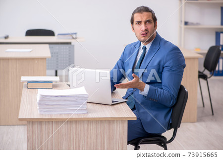 Young male employee and too much work in the office Young male employee and too much work in the office 73915665