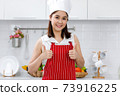 Portrait of happy Asian woman chef in red apron standing in kitchen. 73916225