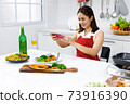 Asian woman in red apron taking a picture of food she make with mobile phone. Concept woman preparing meals at home. 73916390