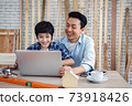 Asian father and son using laptop computer together in carpentry workshop. Concept family doing hobby at home. 73918426