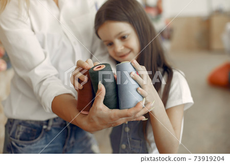 Mother with little daughter standing at the fabric with thread Mother with little daughter standing at the fabric with thread 73919204