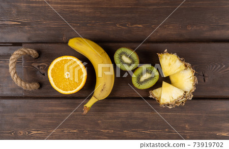 tropical fruits on a wooden background. fresh banana and kiwi. sliced orange and pineapple. tropical fruits on a wooden background. fresh banana and kiwi. sliced orange and pineapple. 73919702