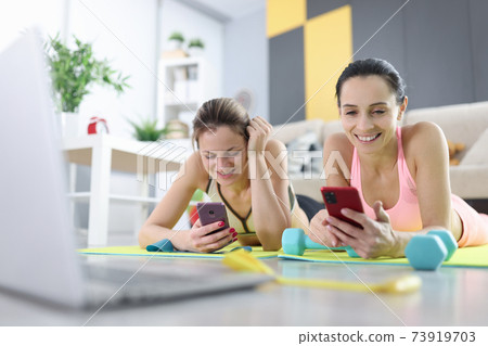 Women in sportswear lying on gymnastic mats with mobile phones 73919703
