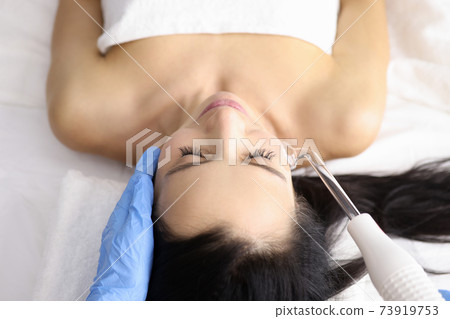 Beautician giving darsonval procedure to young woman in beauty salon Beautician giving darsonval procedure to young woman in beauty salon 73919753