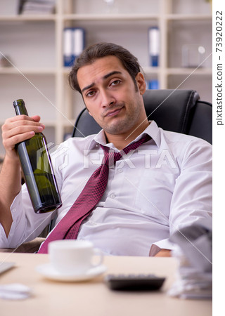 Young male employee drinking alcohol in the office 73920222