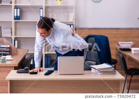 Young male employee suffering from backpain at workplace Young male employee suffering from backpain at workplace 73920472