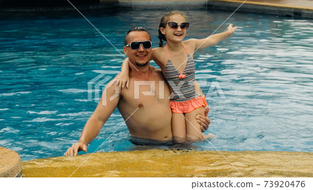 The father with little daughter have fun in the pool. Dad plays with the child. The family enjoy summer vacation in a swimming pool. Slow motion. 73920476