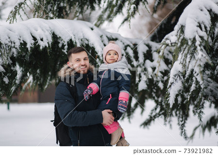 Adorable little daughter with her lovely dad stand by the big snowy tree. Cute little girl laughs Adorable little daughter with her lovely dad stand by the big snowy tree. Cute little girl laughs 73921982