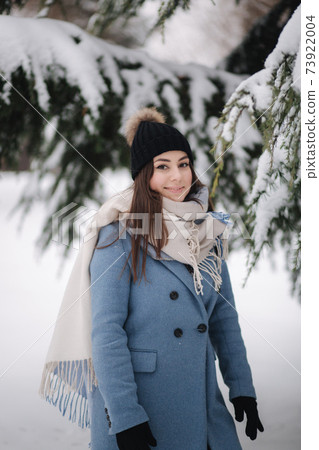 Pretty woman in blue coat walking in the woods on a winter snowy day. Beautiful woman posing to photographer 73922004
