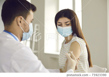 Doctor giving vaccine shot to young woman during immunization campaign at clinic Doctor giving vaccine shot to young woman during immunization campaign at clinic 73923390