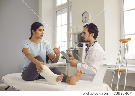 Young woman with leg fracture talking to doctor during medical exam at the clinic Young woman with leg fracture talking to doctor during medical exam at the clinic 73923407