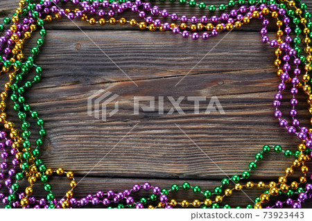 A frame of three colors of Mardi gras beads on wooden background A frame of three colors of Mardi gras beads on wooden background 73923443