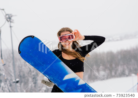 Female in sport wear snowboarder posing in sunglasses with snowboard Female in sport wear snowboarder posing in sunglasses with snowboard 73923540