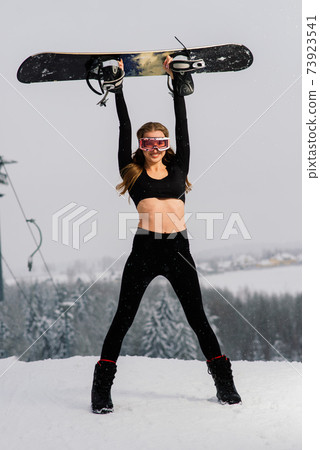Female in sport wear snowboarder posing in sunglasses with snowboard Female in sport wear snowboarder posing in sunglasses with snowboard 73923541