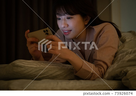 一個女人在一個黑暗的房間裡看著智能手機 73926074