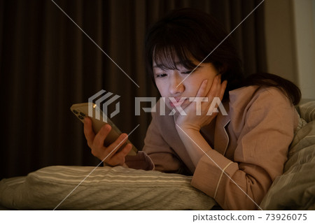 A woman who is depressed looking at a smartphone in a dark room 73926075