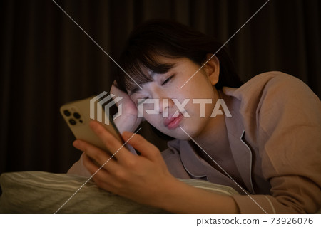 一個女人在一個黑暗的房間裡看著智能手機 73926076