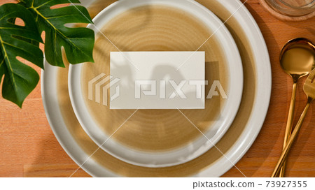 Dining set with mock up name card on mock up ceramic plate and brass spoon and fork Dining set with mock up name card on mock up ceramic plate and brass spoon and fork 73927355