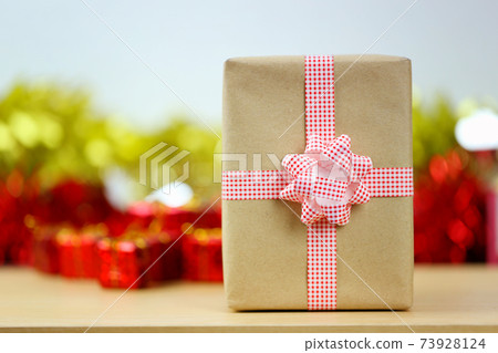 A brown gift box is placed on a table with festive decorations item. A brown gift box is placed on a table with festive decorations item. 73928124