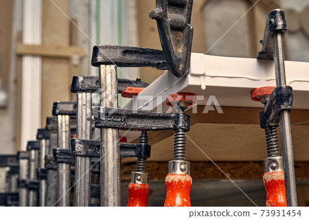 Joinery. Gluing and clamping table top of acrylic stone. Production of wood furniture. Furniture manufacture. Close-up Joinery. Gluing and clamping table top of acrylic stone. Production of wood furniture. Furniture manufacture. Close-up 73931454
