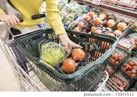 A female shopper who puts tomatoes in a shopping cart at a supermarket A female shopper who puts tomatoes in a shopping cart at a supermarket 73933513