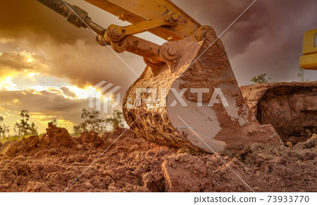 Dirt metal bucket of backhoe after digging soil. Backhoe parked at agricultural land on sunset sky background. Crawler excavator. Earthmoving machine at construction site at dusk. Excavation vehicle. Dirt metal bucket of backhoe after digging soil. Backhoe parked at agricultural land on sunset sky background. Crawler excavator. Earthmoving machine at construction site at dusk. Excavation vehicle. 73933770