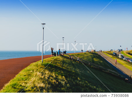 Westkapelle, The Netherlands, August 2019. The built-up area, below sea level, is protected by an artificial hill that surrounds it. On the top of the hill a red road. Westkapelle, The Netherlands, August 2019. The built-up area, below sea level, is protected by an artificial hill that surrounds it. On the top of the hill a red road. 73938086