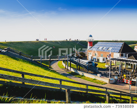 Westkapelle, The Netherlands, August 2019. The built-up area, below sea level, is protected by an artificial hill that surrounds it. On the top of the hill a red road. Westkapelle, The Netherlands, August 2019. The built-up area, below sea level, is protected by an artificial hill that surrounds it. On the top of the hill a red road. 73938089