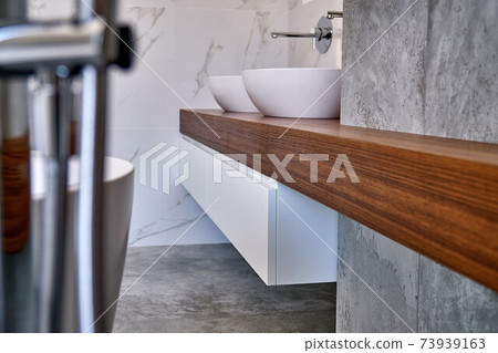 Luxury floating bathroom vanity. Stylish interior of modern bathroom teak tabletop and marble walls Luxury floating bathroom vanity. Stylish interior of modern bathroom teak tabletop and marble walls 73939163