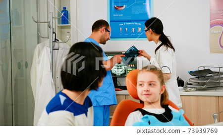 Team of stomatologist doctors analysing teeth x-ray of little patient Team of stomatologist doctors analysing teeth x-ray of little patient 73939769