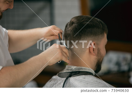 Close up master barber, stylist does the hairstyle to guy, young man. Professional occupation, male beauty concept 73940630