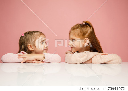 Happy kids, girls isolated on coral pink studio background. Look happy, cheerful, sincere. Copyspace. Childhood, education, emotions concept 73941972