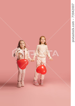 Happy kids, girls isolated on coral pink studio background. Look happy, cheerful, sincere. Copyspace. Childhood, education, emotions concept 73942007
