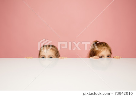 Happy kids, girls isolated on coral pink studio background. Look happy, cheerful, sincere. Copyspace. Childhood, education, emotions concept 73942010