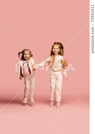 Happy kids, girls isolated on coral pink studio background. Look happy, cheerful, sincere. Copyspace. Childhood, education, emotions concept Happy kids, girls isolated on coral pink studio background. Look happy, cheerful, sincere. Copyspace. Childhood, education, emotions concept 73942011
