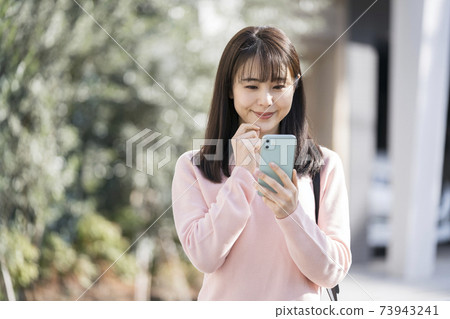 A smiling young woman looking at a smartphone screen 73943241