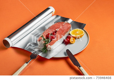 fresh salmon with lemon in foil paper, ready for cooking in oven on orange background fresh salmon with lemon in foil paper, ready for cooking in oven on orange background 73946408