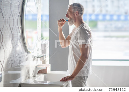 Gray-haired man brushing teeth in morning. Gray-haired man brushing teeth in morning. 73948112